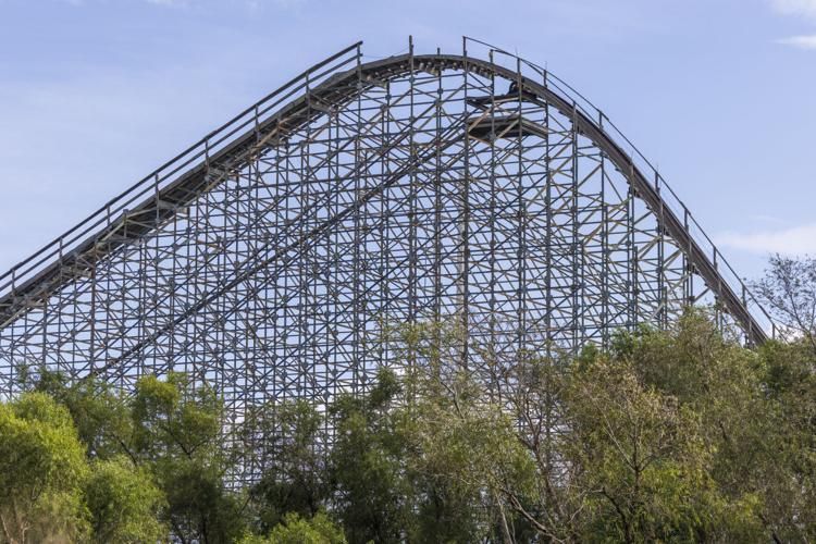 An unused roller coaster rises up behind dense trees at the former Six Flags site.